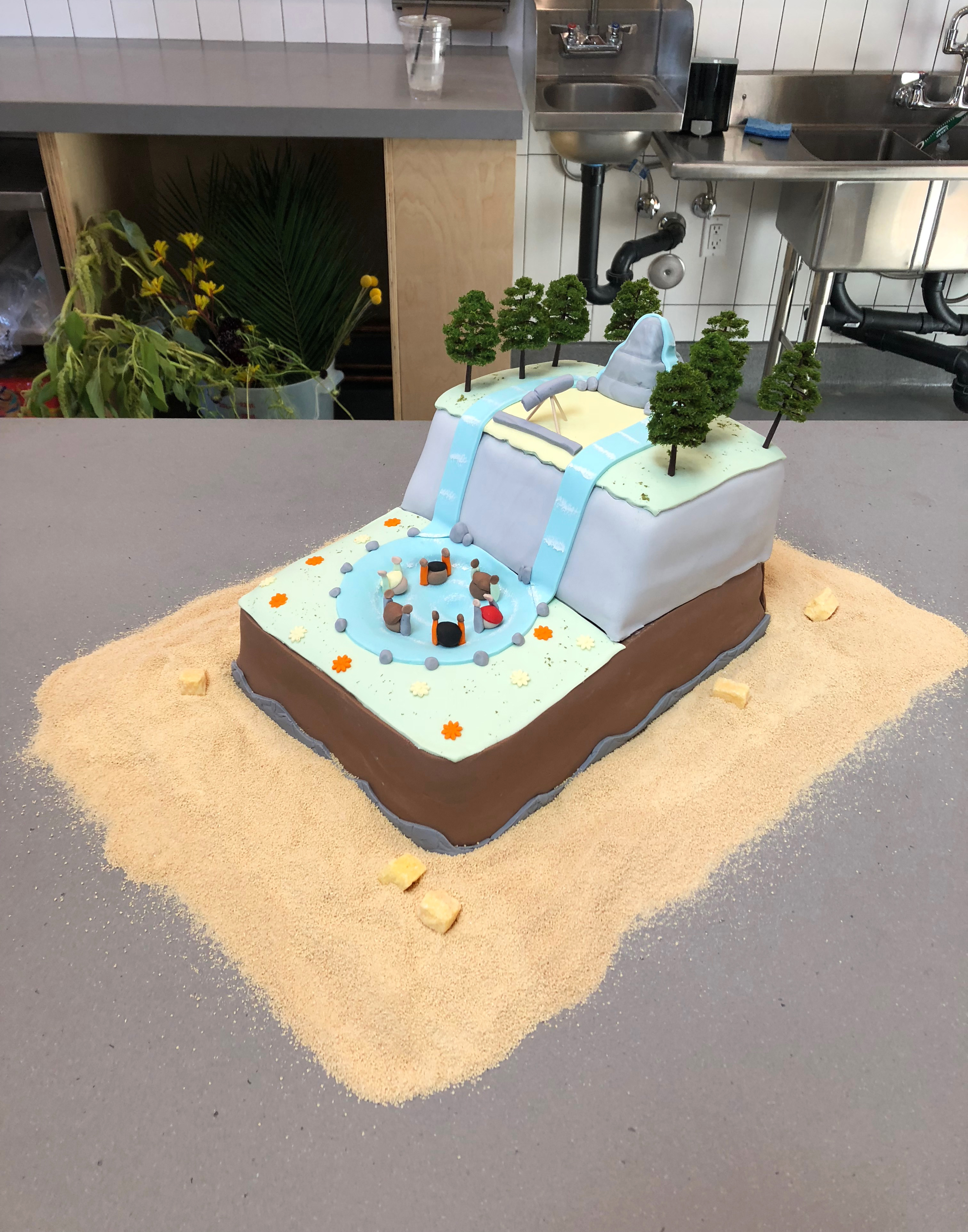 A sculptural cake depicting a landscape with a whirlpool full of drowning people on a gray countertop